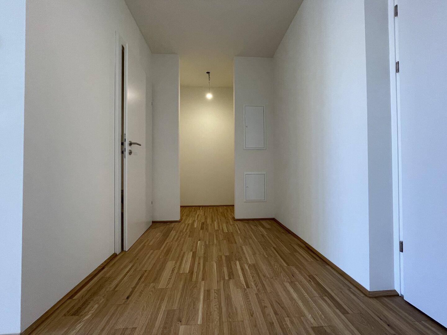 Heller Flur mit Eichenparkettboden und weißen Wänden, der zu weiteren Räumen führt.