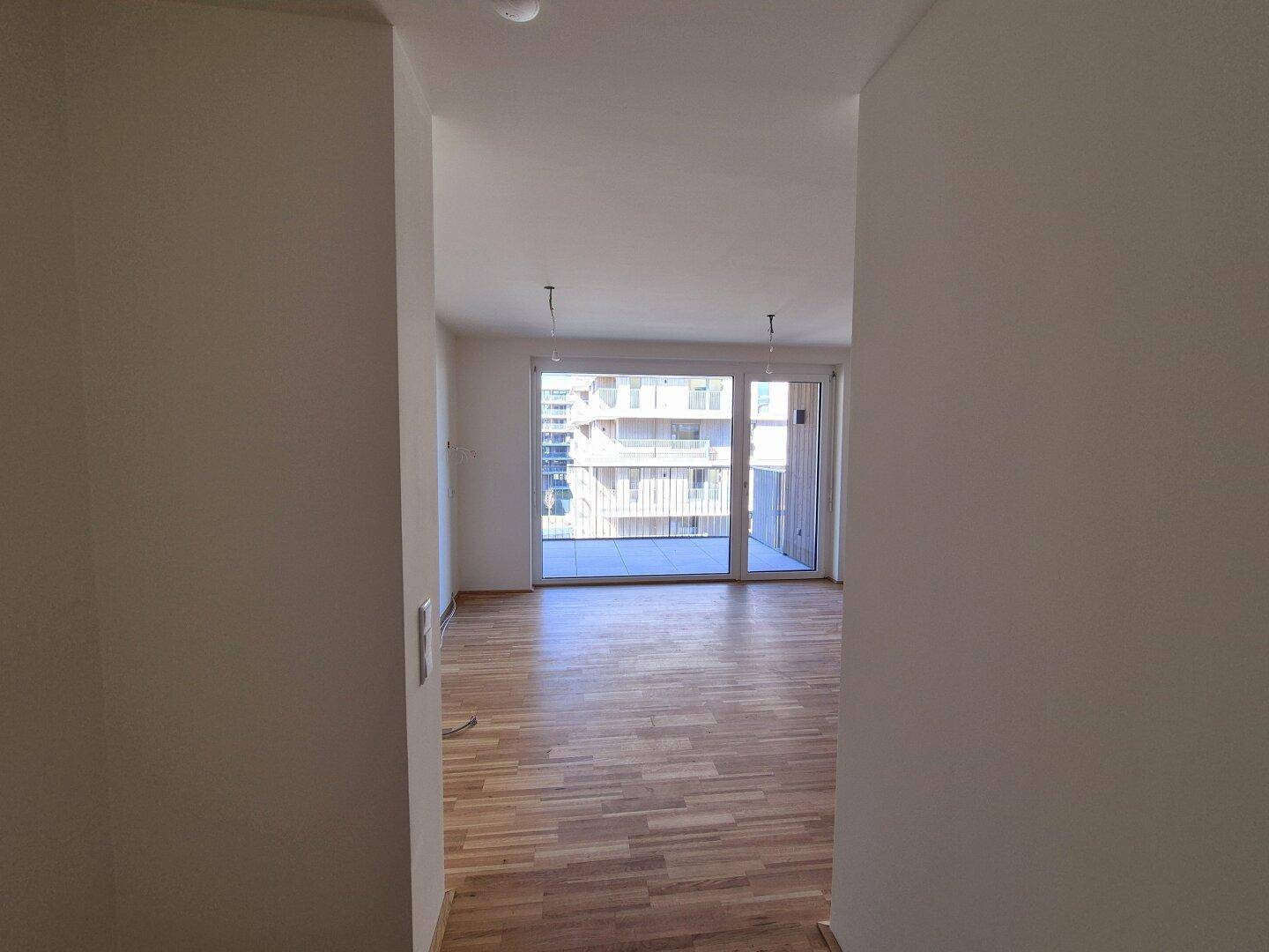 Heller, leerer Raum mit Parkettboden und großem Fenster mit Zugang zum Balkon.