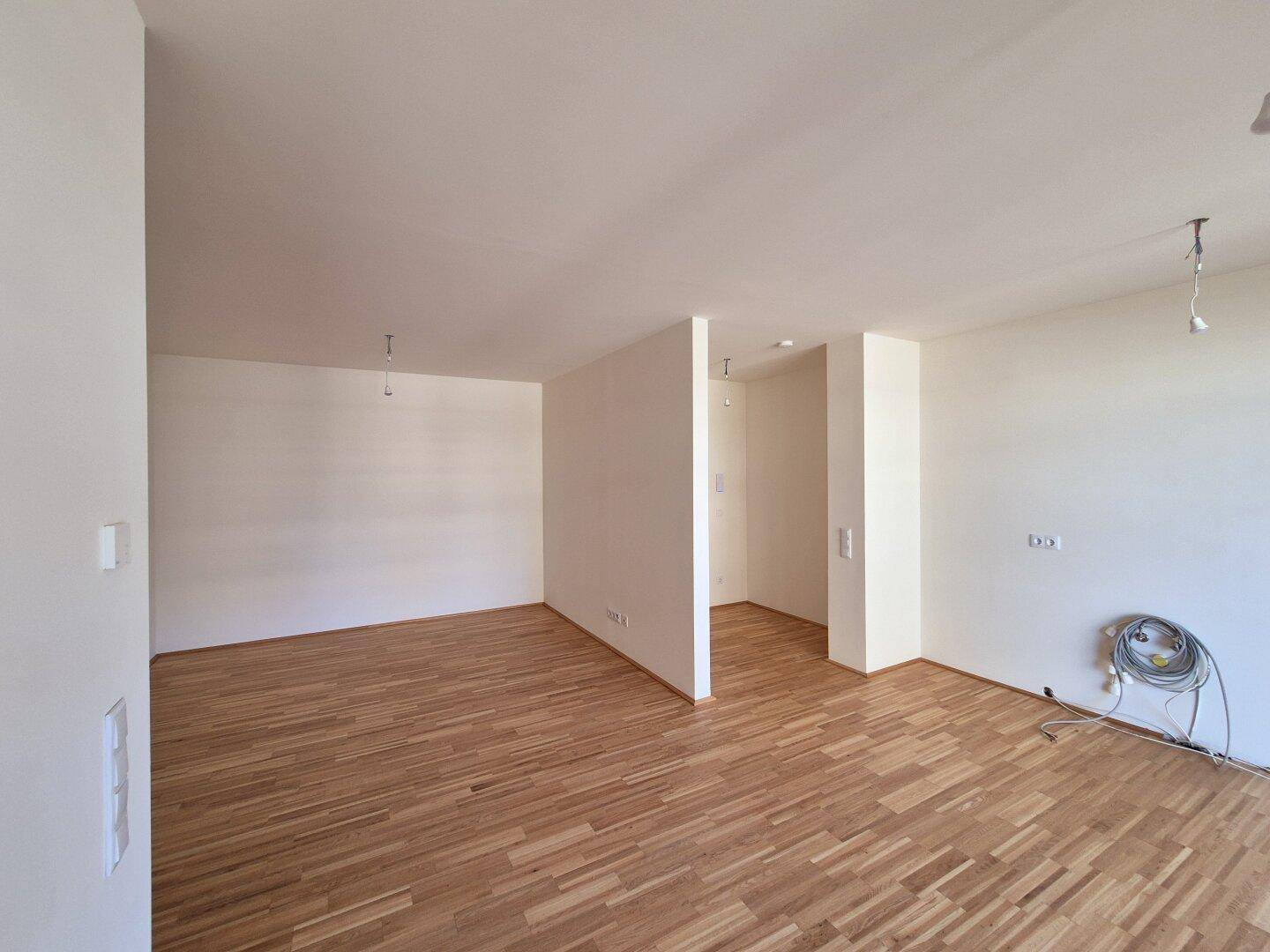 Geräumiger, heller Wohnbereich mit Parkettboden und weißen Wänden, bereit zur individuellen Gestaltung.