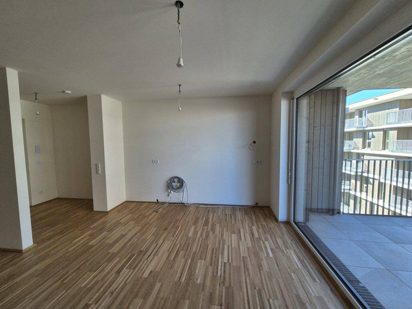 Lichtdurchfluteter Wohnbereich mit Parkettboden und direktem Zugang zu einem großen Balkon.