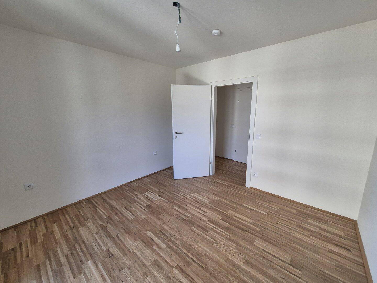 Leeres Schlafzimmer mit hellem Parkettboden und weiß gestrichenen Wänden, bereit zum Einzug.