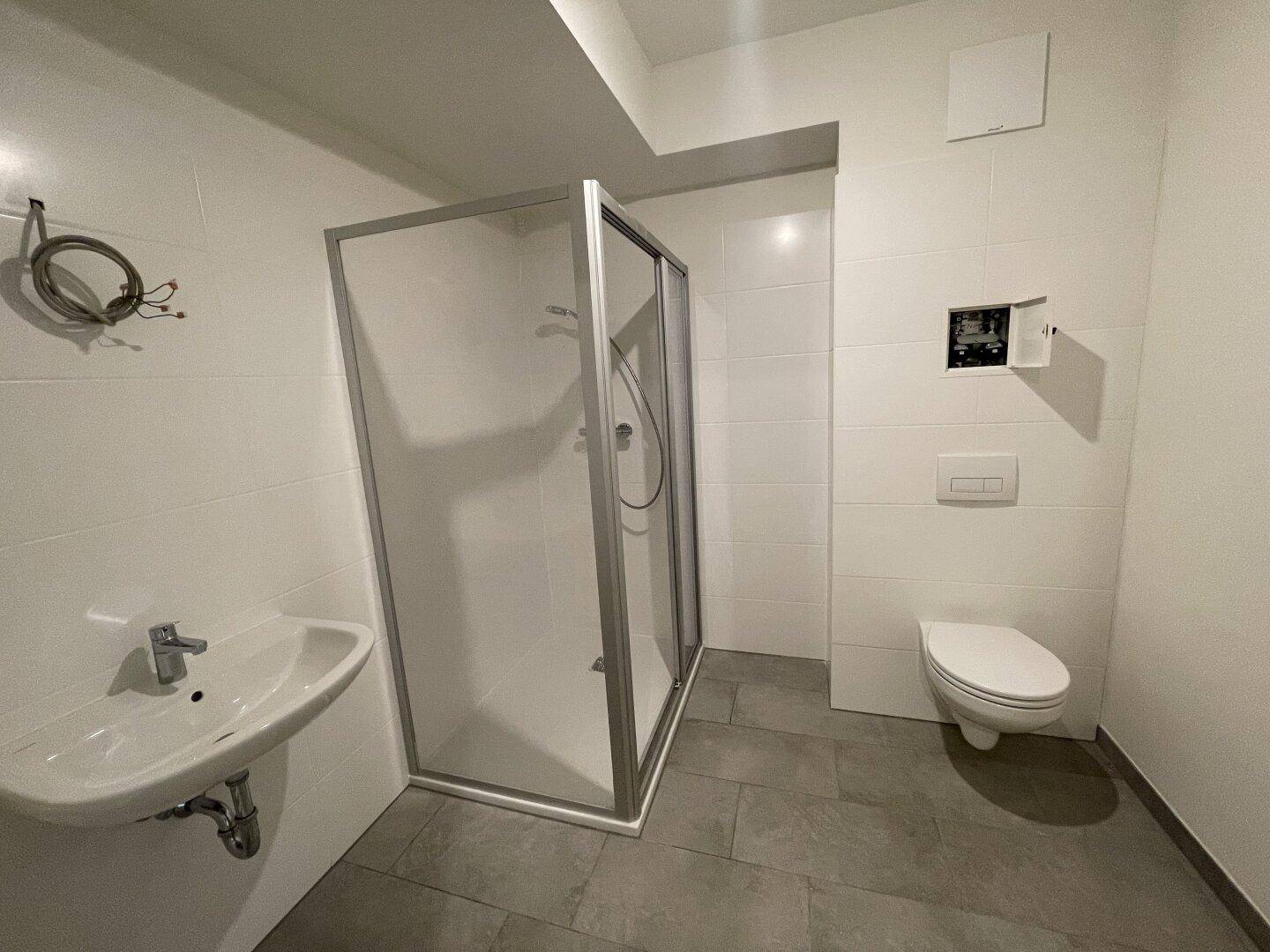 Modernes Badezimmer mit Duschkabine, Wand-WC und Waschbecken in hellen Fliesen.