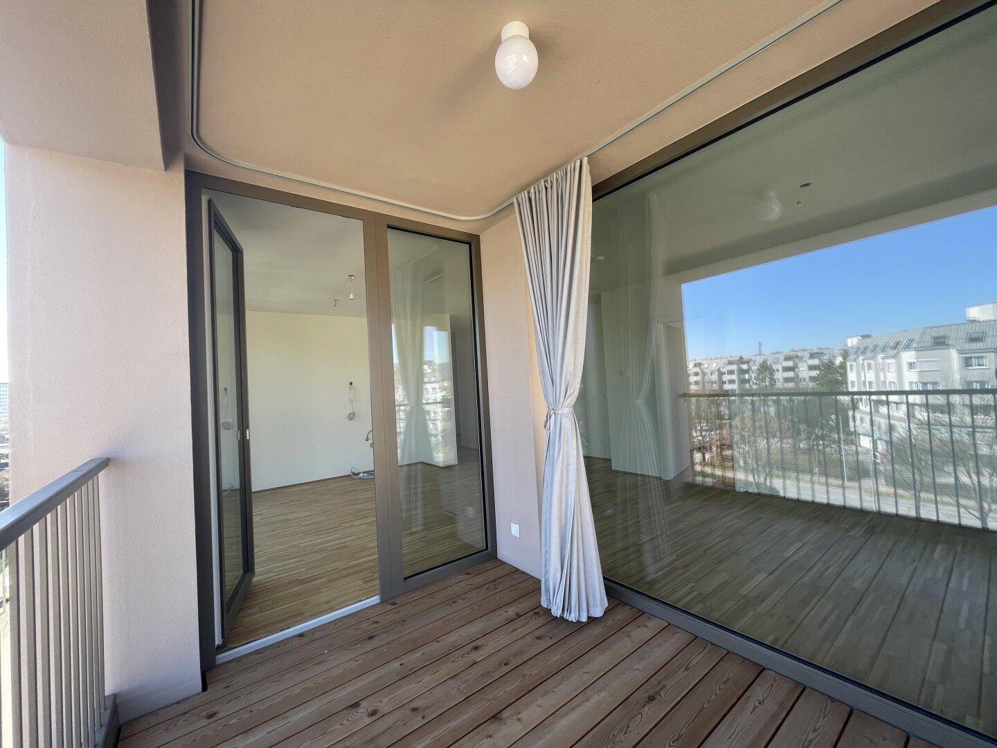 Balkon mit Holzboden und Zugang zu einem leeren Raum, der viel Tageslicht erhält.