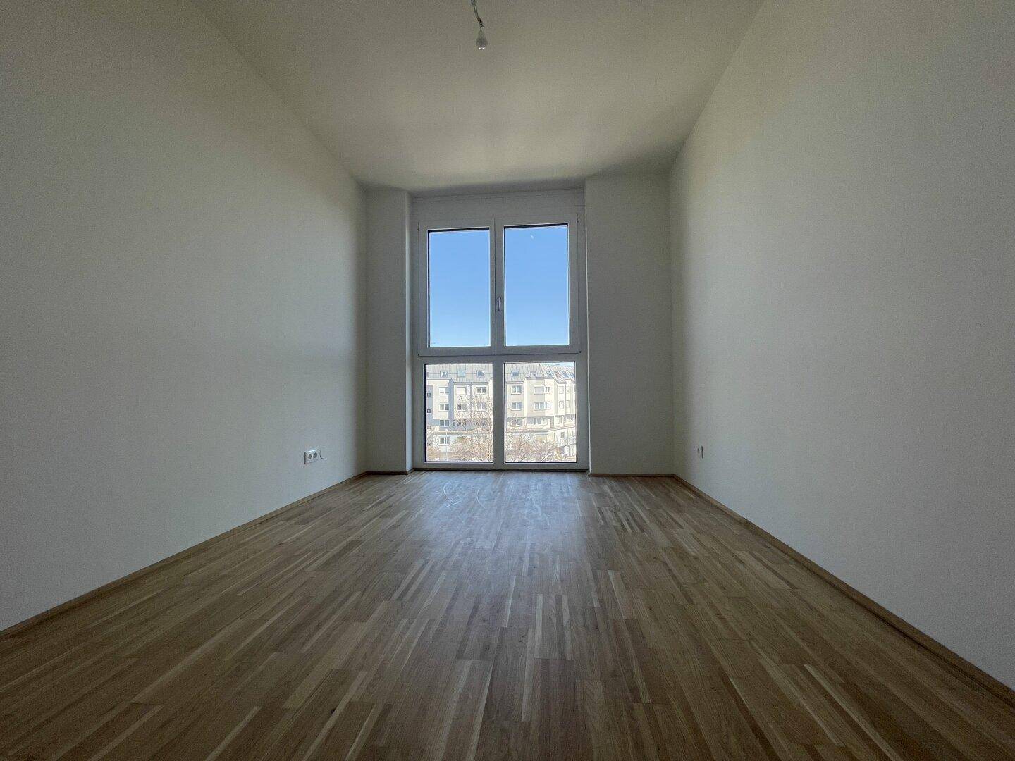 Geräumiges Schlafzimmer mit Parkettboden und Fenster mit Blick auf die Umgebung.