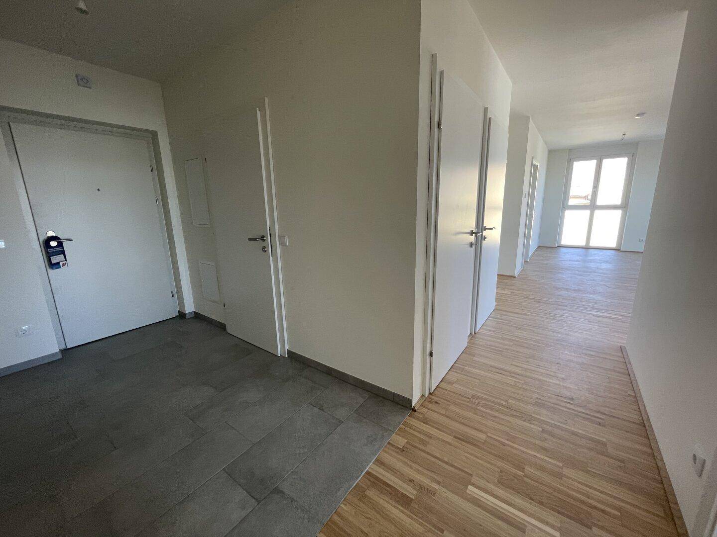 Heller Eingangsbereich mit Fliesenboden, der in Parkett übergeht, und mehreren Türen.