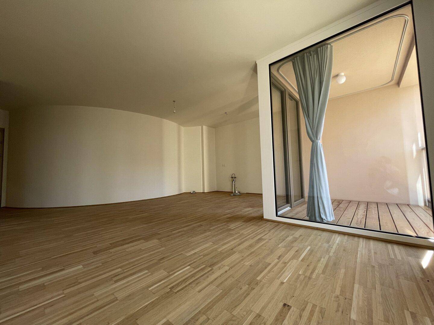 Heller Wohnbereich mit Holzboden und großen Fenstern, die viel Tageslicht hereinlassen.