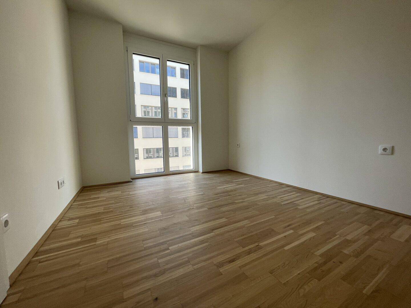 Helles Zimmer mit Parkettboden und großem Fenster, ideal als Schlaf- oder Arbeitszimmer.