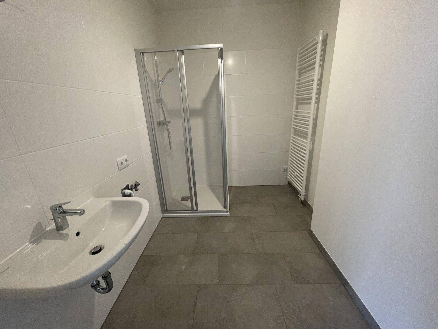 Modernes Badezimmer mit Dusche, Waschbecken und weiß gefliesten Wänden.