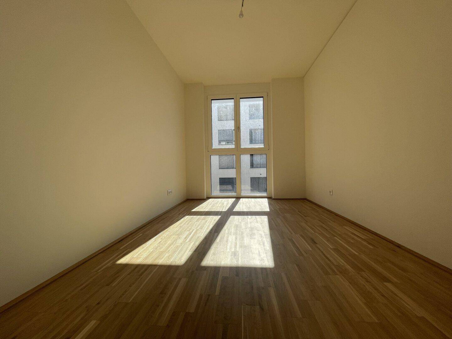Sonniger Raum mit Parkettboden und großem Fenster, bietet viel Potenzial für ein Schlafzimmer.