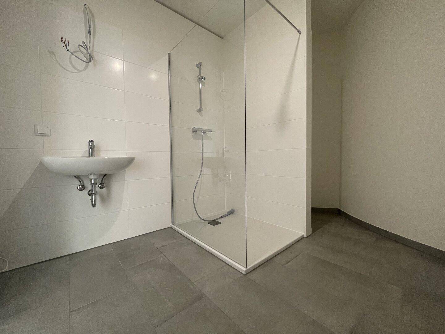Modernes Badezimmer mit ebenerdiger Dusche, weißen Fliesen und grauem Boden.
