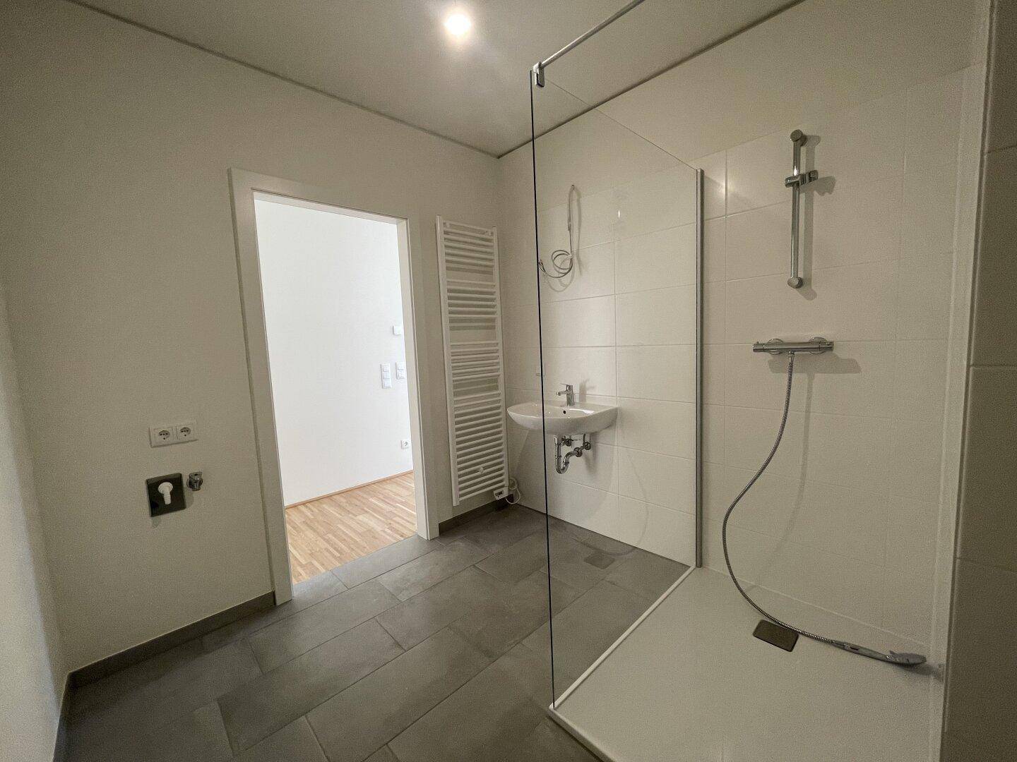 Helles Badezimmer mit moderner Dusche, Handtuchheizkörper und Zugang zu einem weiteren Raum.