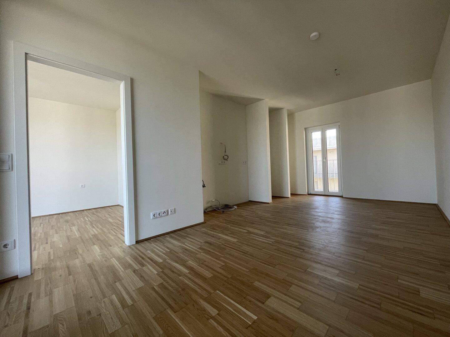 Helles, leeres Zimmer mit Parkettboden und Zugang zu einem weiteren Raum.
