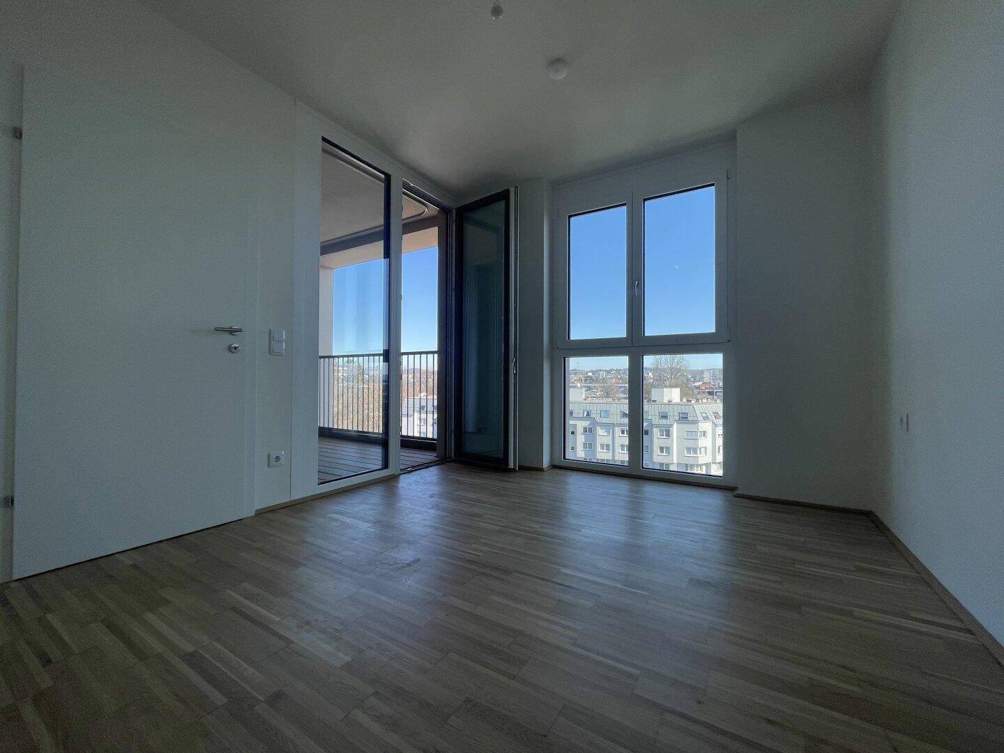 Helles Schlafzimmer mit Parkettboden, großen Fenstern und Zugang zum Balkon.