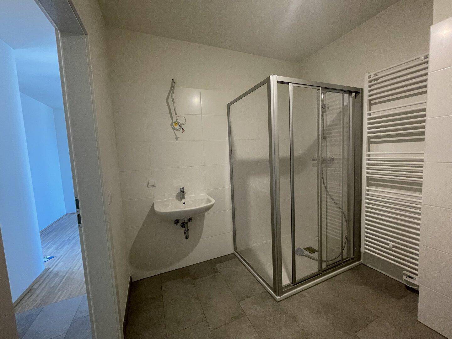 Modernes Badezimmer mit Duschkabine, Waschbecken und Handtuchheizkörper.