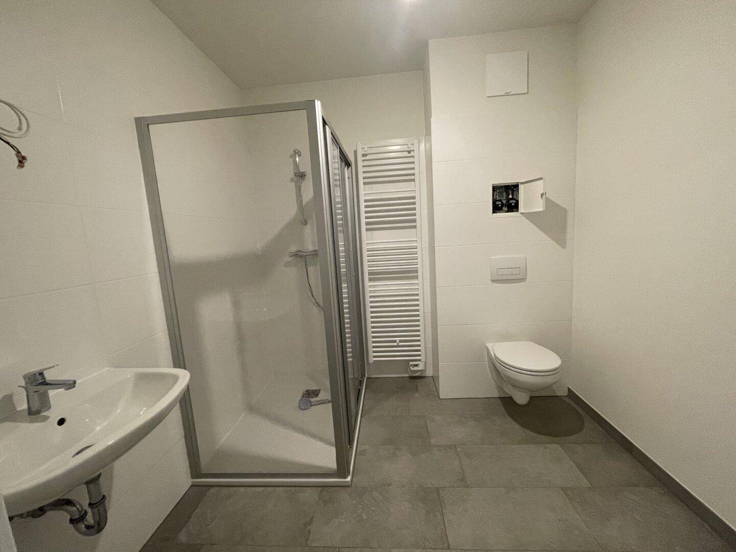 Funktionales Badezimmer mit Duschkabine, wandhängendem WC und Heizkörper.