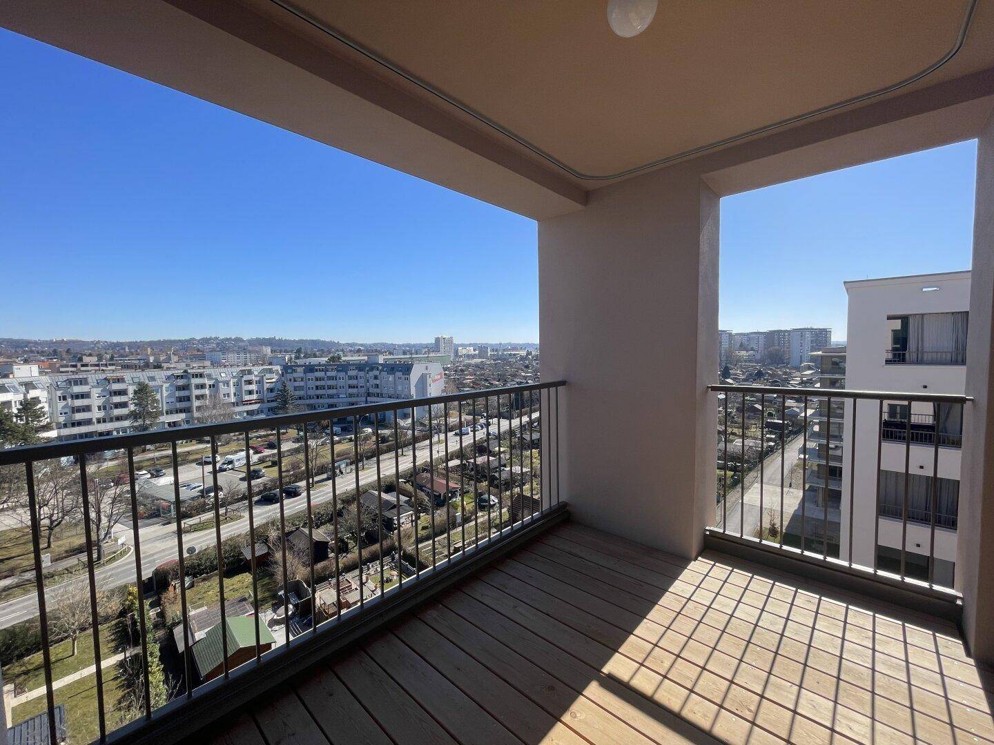 Heller Balkon mit Holzdielen und Panoramablick auf die umliegende Stadtlandschaft.