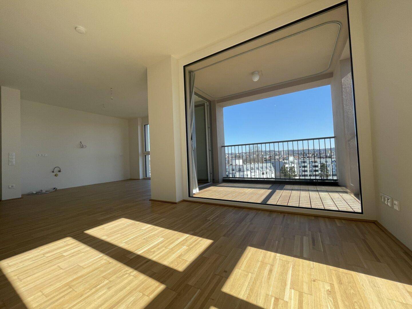 Geräumiger Wohnbereich mit Parkettboden und direktem Zugang zu einem sonnigen Balkon.