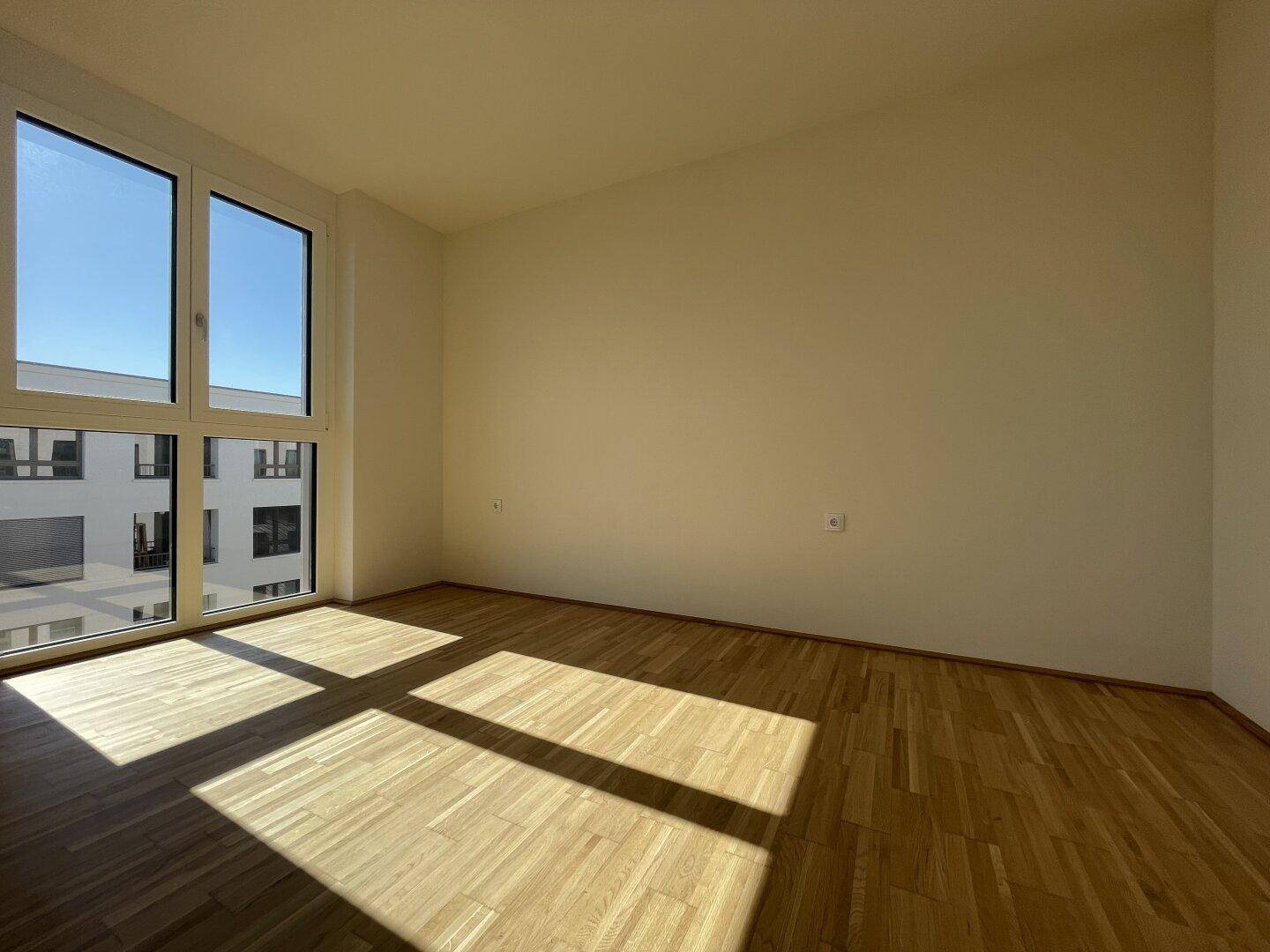 Helles Schlafzimmer mit Parkettboden und großem Fenster, das viel Tageslicht hereinlässt.
