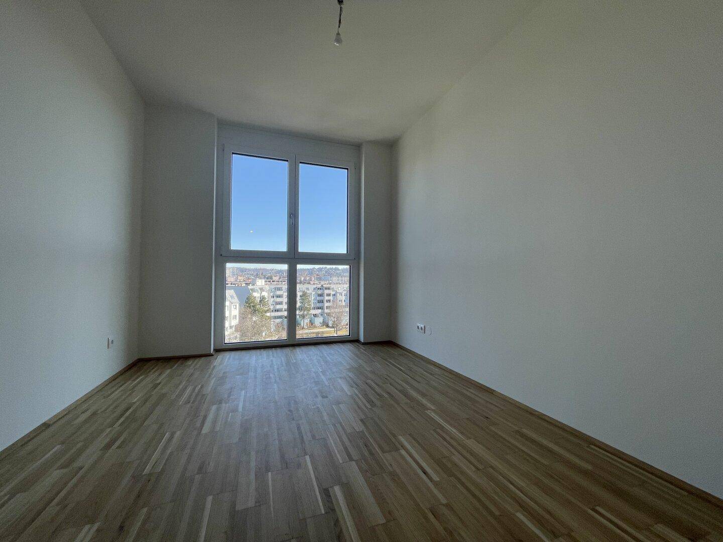 Ruhiges Schlafzimmer mit Parkettboden und Fenster mit Blick auf die Stadt.