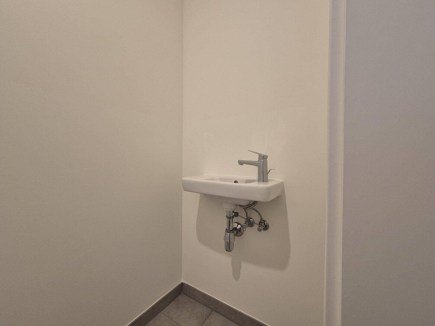 Modernes wandmontiertes Waschbecken in einem kleinen WC-Raum mit Fliesenboden.