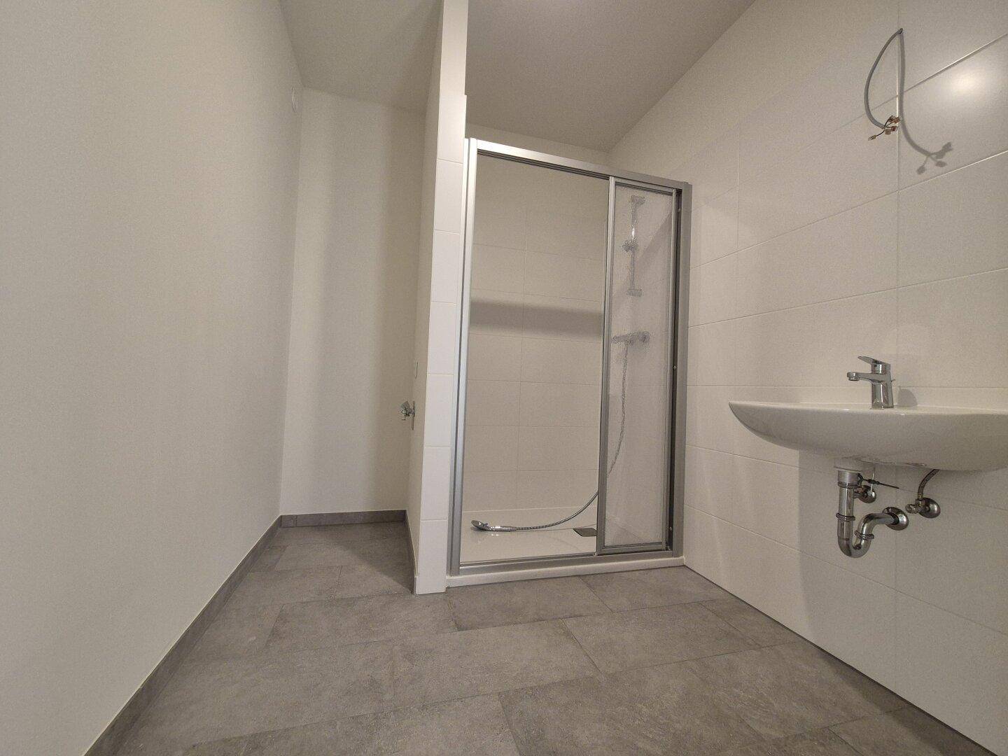 Modernes Badezimmer mit Duschkabine, Waschbecken und grauen Bodenfliesen.