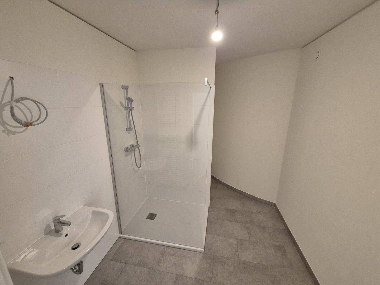 Modernes Badezimmer mit Duschkabine, grauen Fliesen und weißer Wandverkleidung.