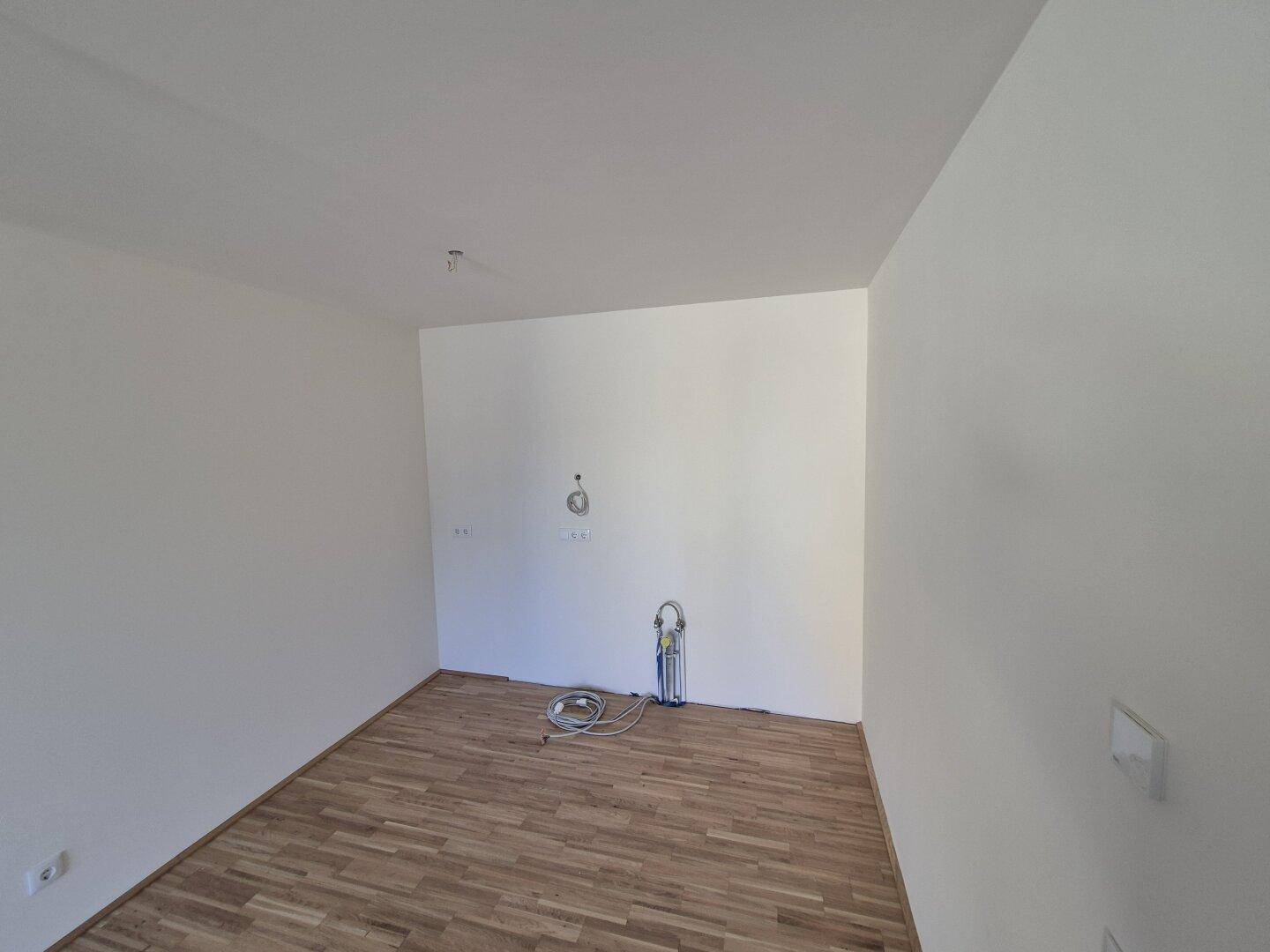 Leerer Küchenbereich mit Anschlüssen für eine Einbauküche und hellem Holzboden.