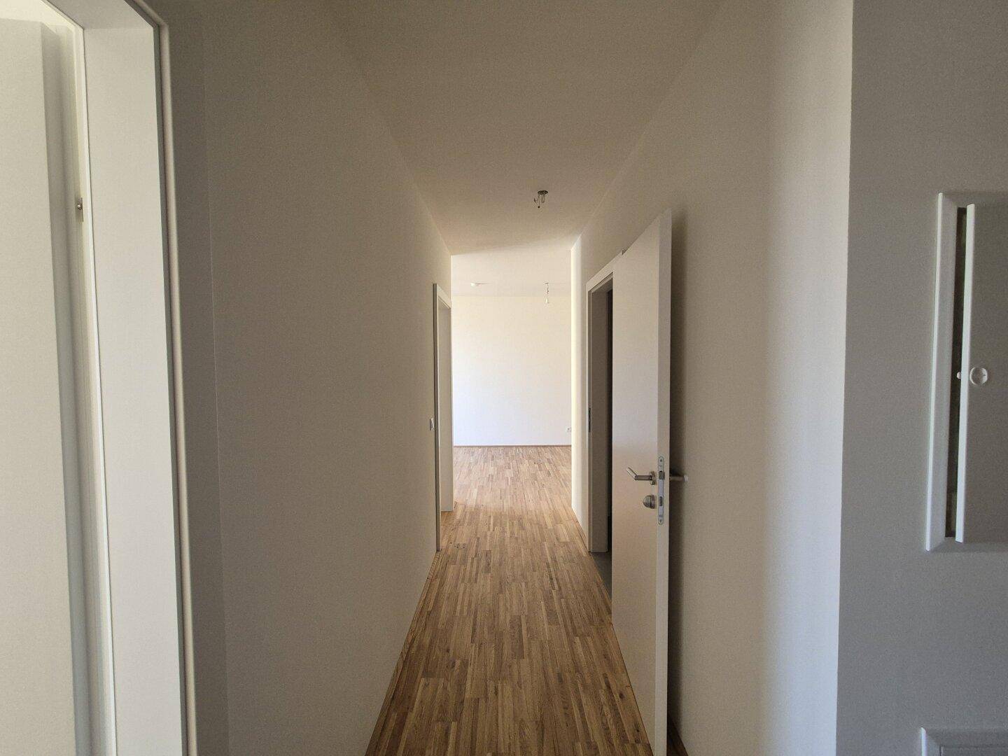 Langer, heller Flur mit Holzboden, der zu weiteren Räumen in der Wohnung führt.