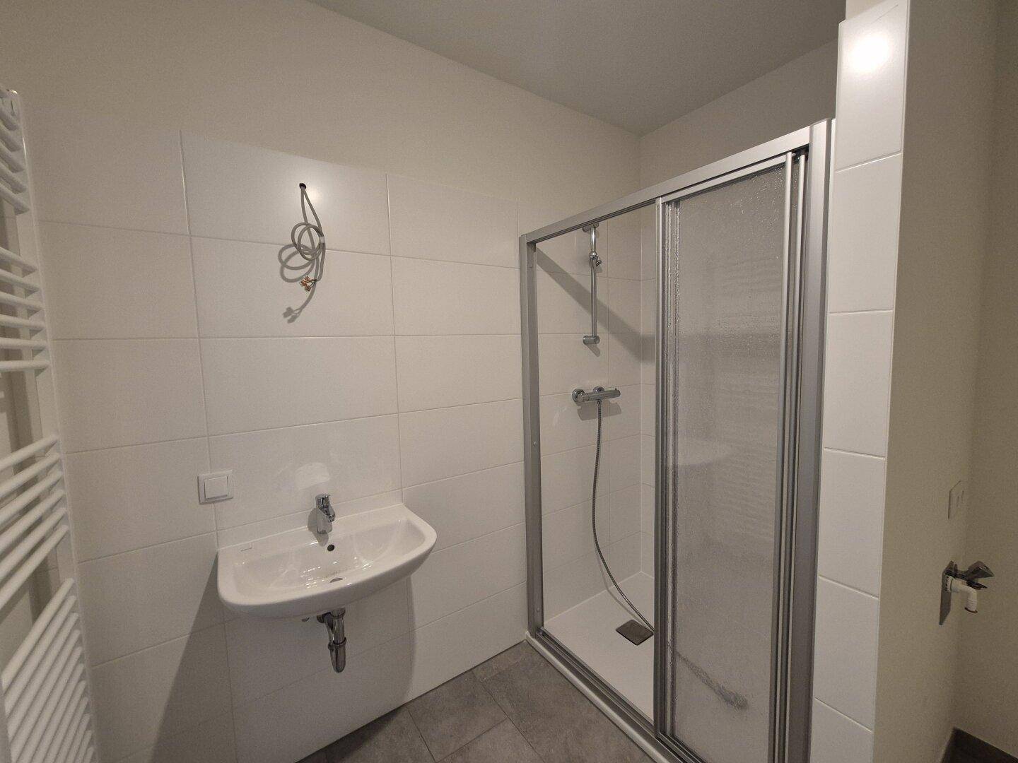 Modernes Badezimmer mit Duschkabine, Waschbecken, beheiztem Handtuchhalter und weißen Fliesen.