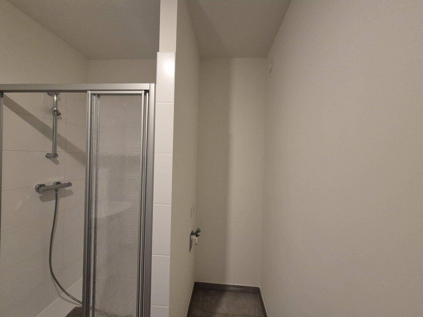 Teilansicht eines Badezimmers mit Duschbereich und vorbereiteten Anschlüssen für weitere Installationen.