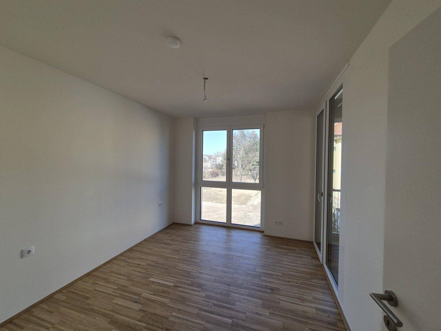 Helles Zimmer mit Holzboden und großem Fenster, das viel Tageslicht hereinlässt.