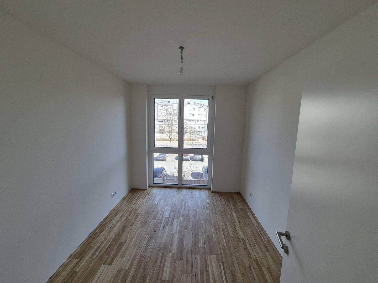 Helles Schlafzimmer mit Holzboden und großem Fenster mit Blick nach draußen.