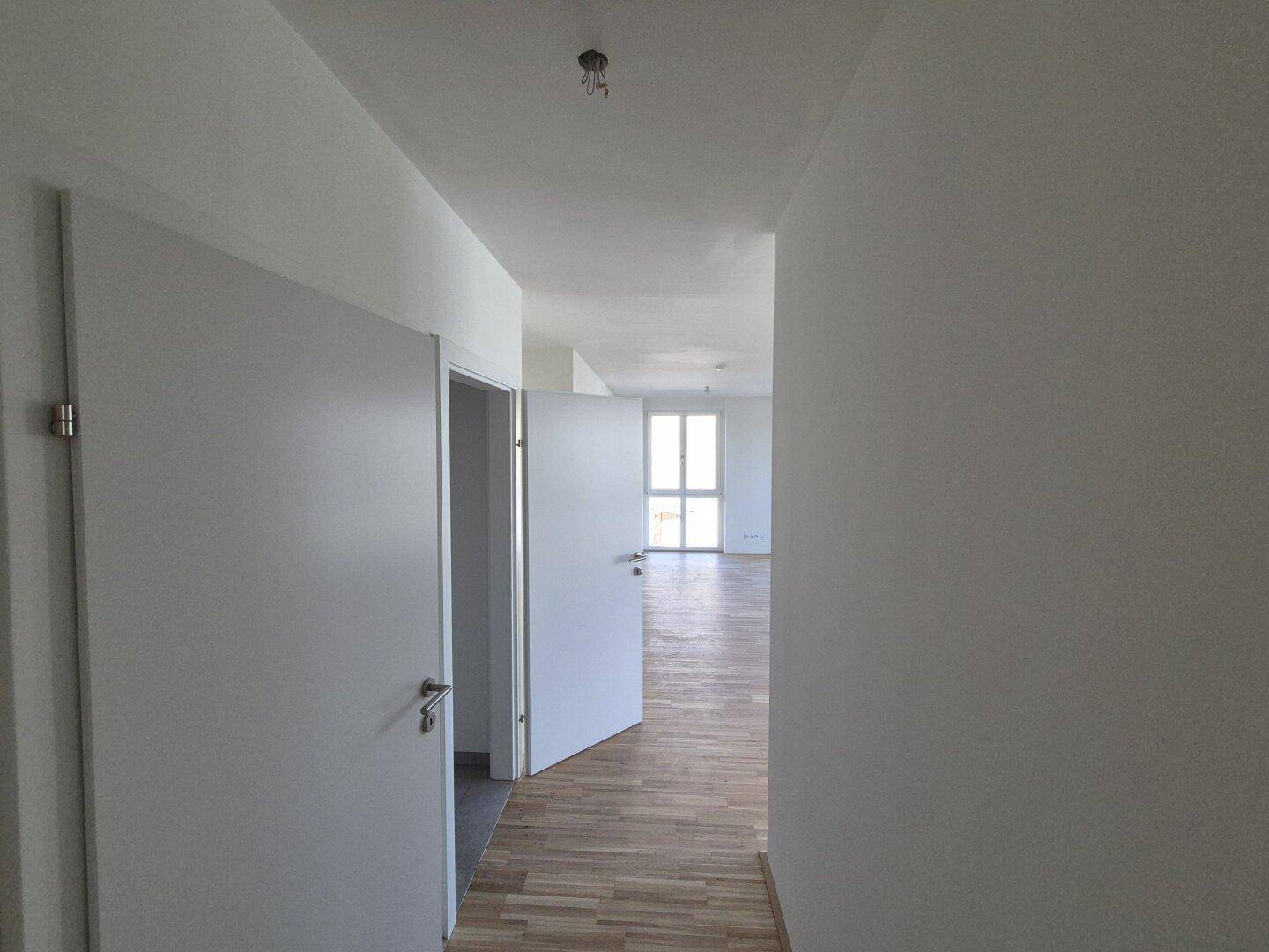 Heller Flur mit Holzboden und weißen Türen, der zu weiteren Räumen führt.