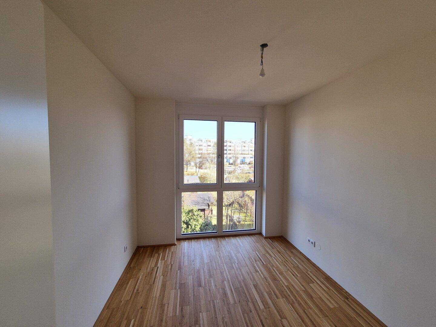 Helles Zimmer mit Holzboden und großem Fenster, bietet einen weiten Blick nach draußen.