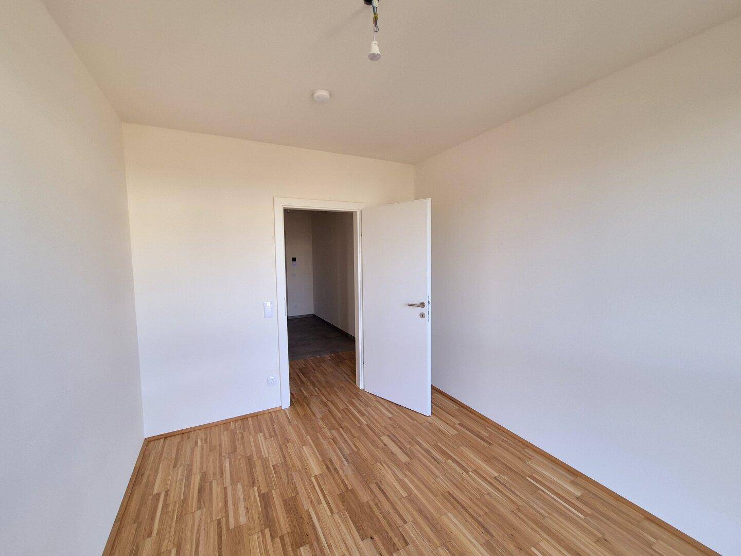 Leeres Zimmer mit Holzboden und weiß gestrichenen Wänden, ideal für Schlaf- oder Arbeitszimmer.