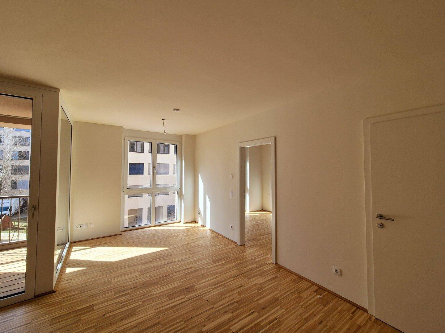 Heller Wohnraum mit Parkettboden und Blick auf die umliegenden modernen Gebäude.