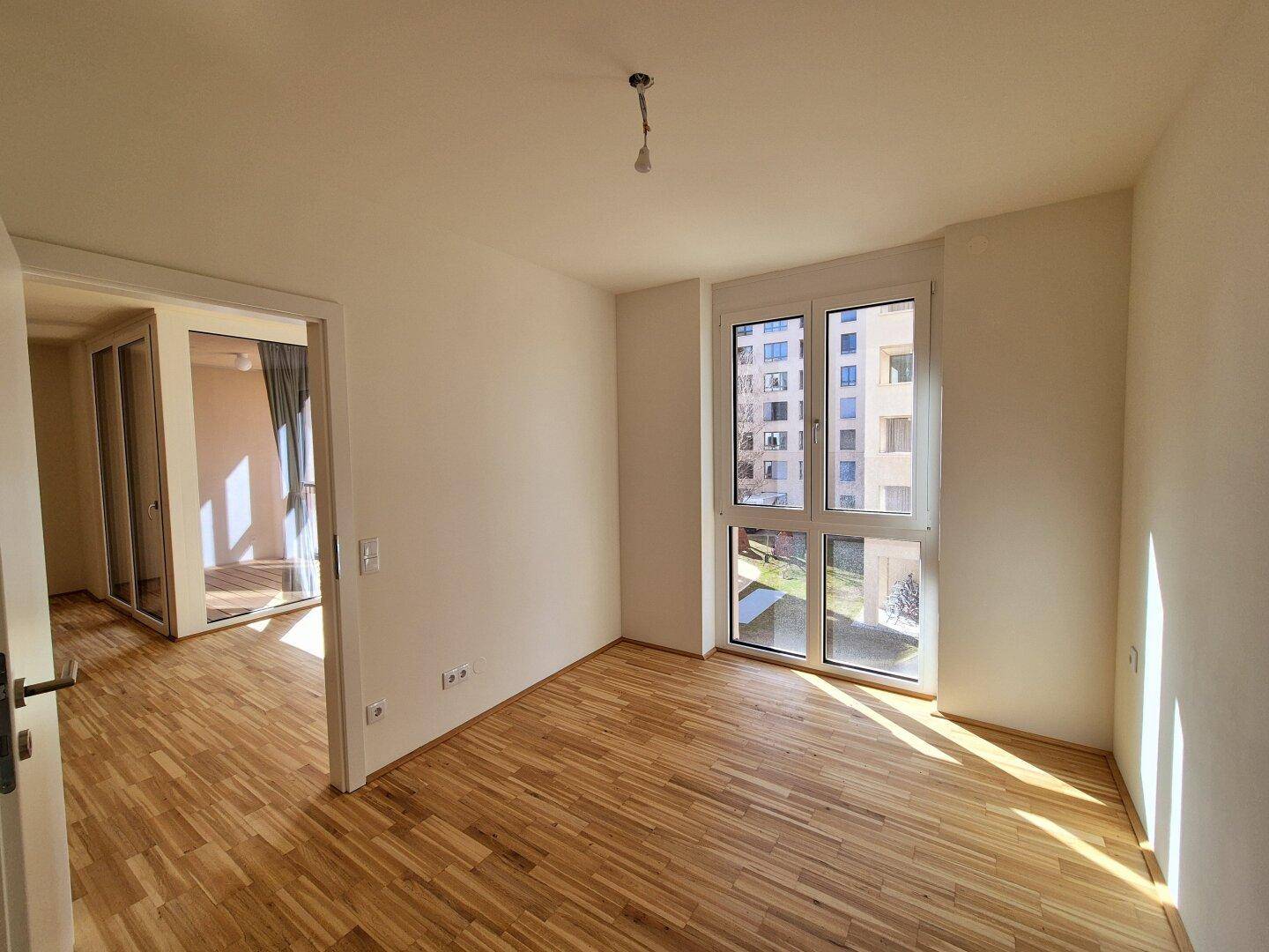 Helles Zimmer mit Parkettboden und großem Fenster, ideal als Schlaf- oder Arbeitszimmer.