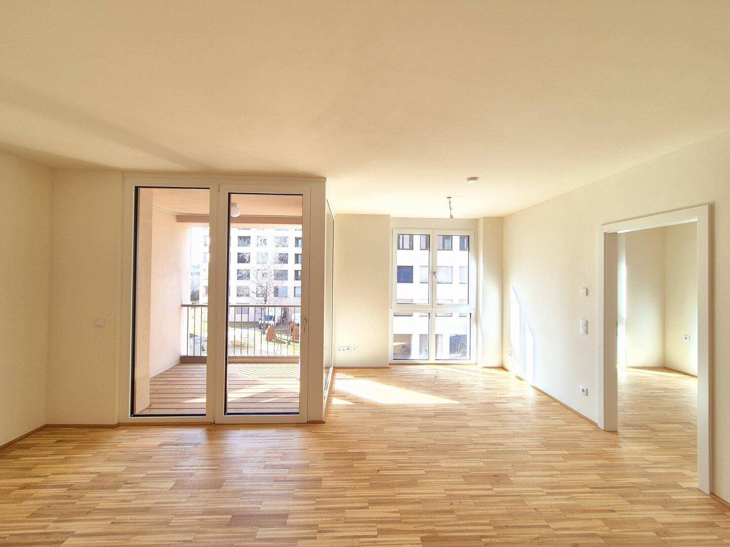 Lichtdurchfluteter Wohnbereich mit Parkettboden und großen Fenstern, die viel Tageslicht hereinlassen.