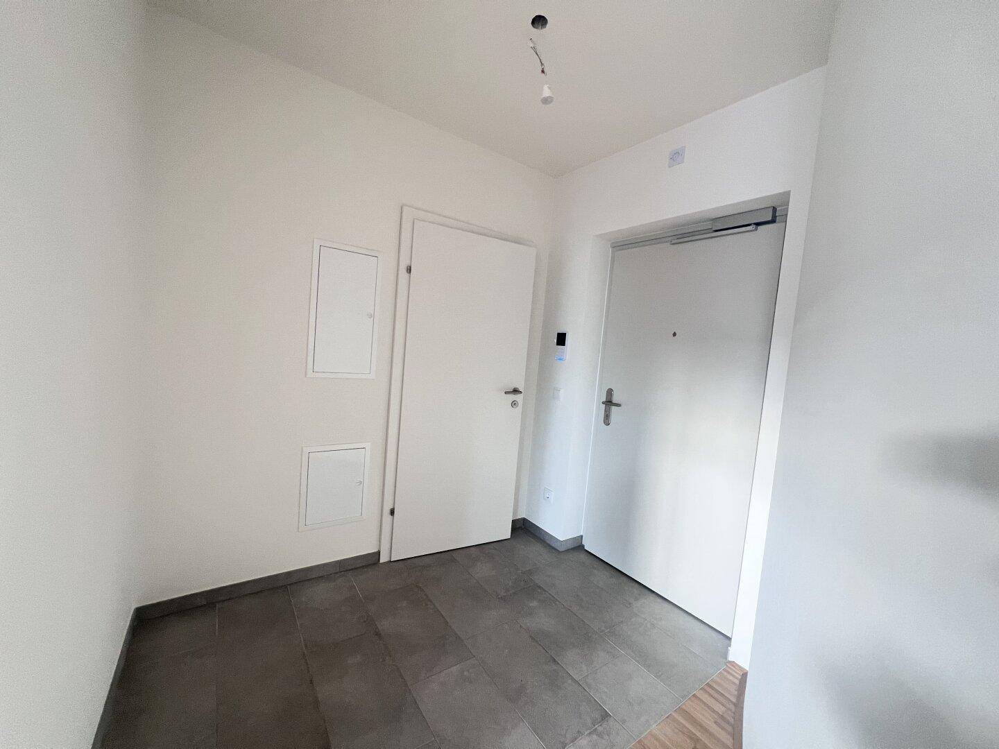 Heller Eingangsbereich mit Fliesenboden und zwei Türen in einem modernen Neubau.