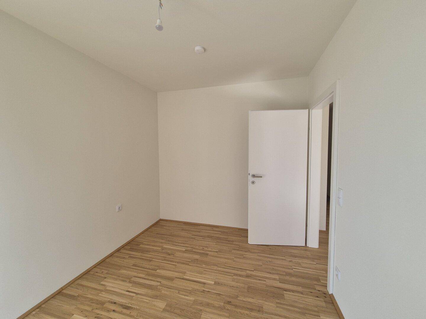 Leeres Zimmer mit hellem Parkettboden und weißen Wänden, bereit für individuelle Gestaltung.