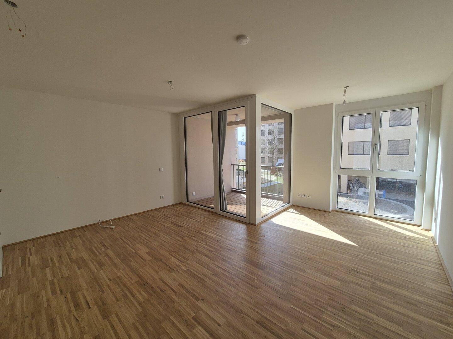 Lichtdurchfluteter Wohnraum mit Parkettboden, großen Fenstern und direktem Balkonzugang.