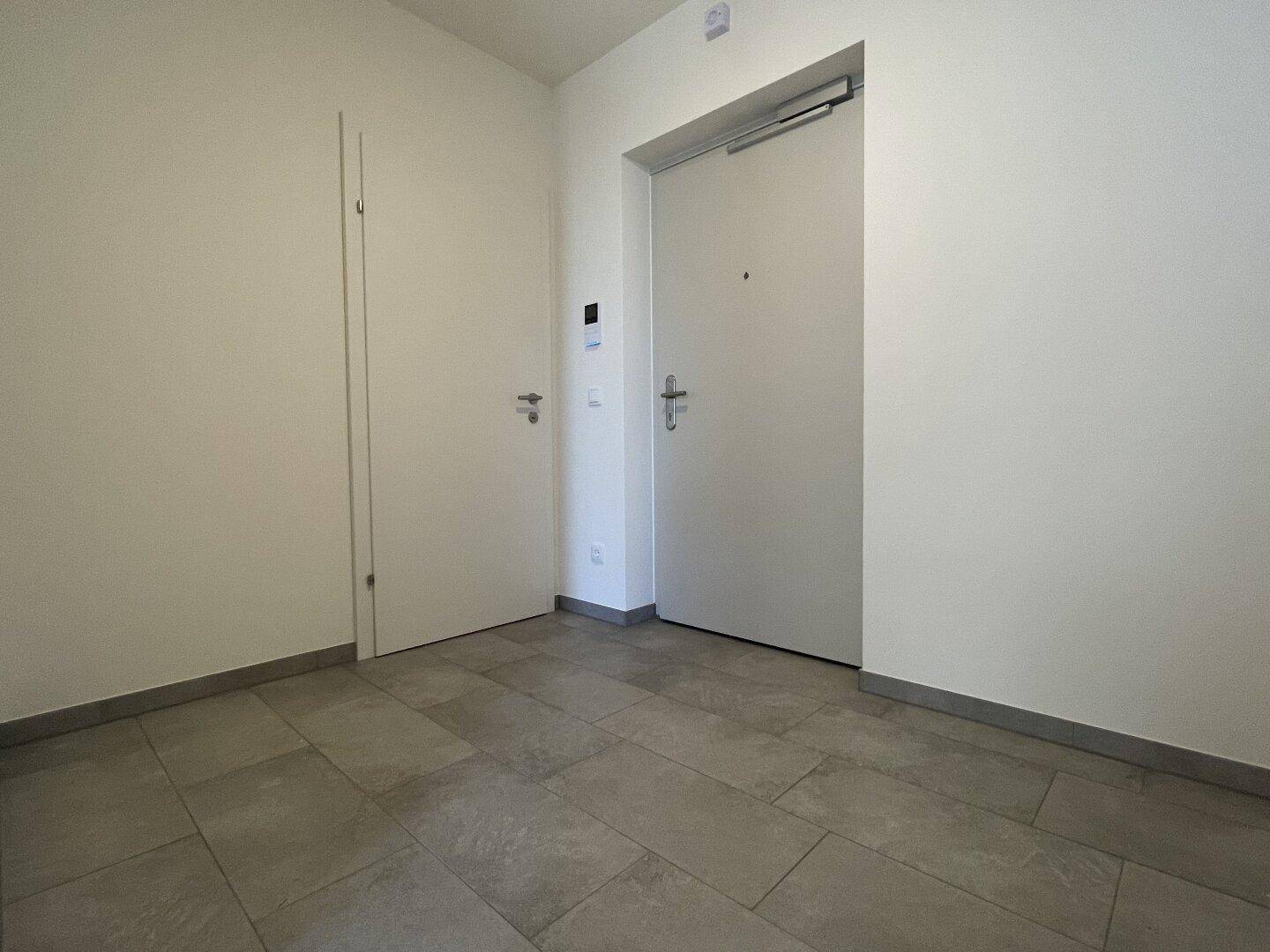 Heller Eingangsbereich mit Fliesenboden und weißer Wohnungstür in einem modernen Neubau.