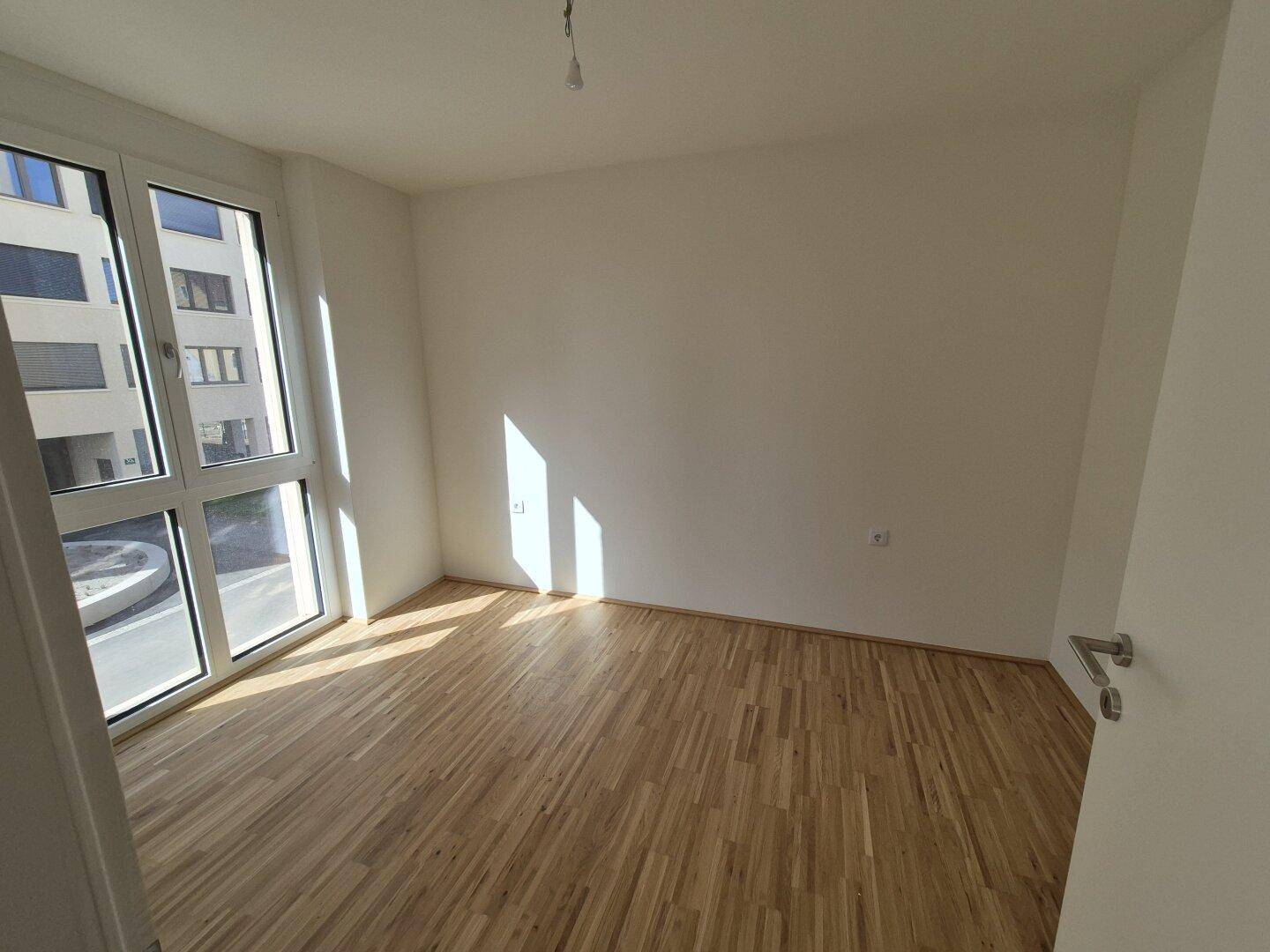 Helles Schlafzimmer mit Parkettboden und großen Fenstern, die viel Tageslicht hereinlassen.