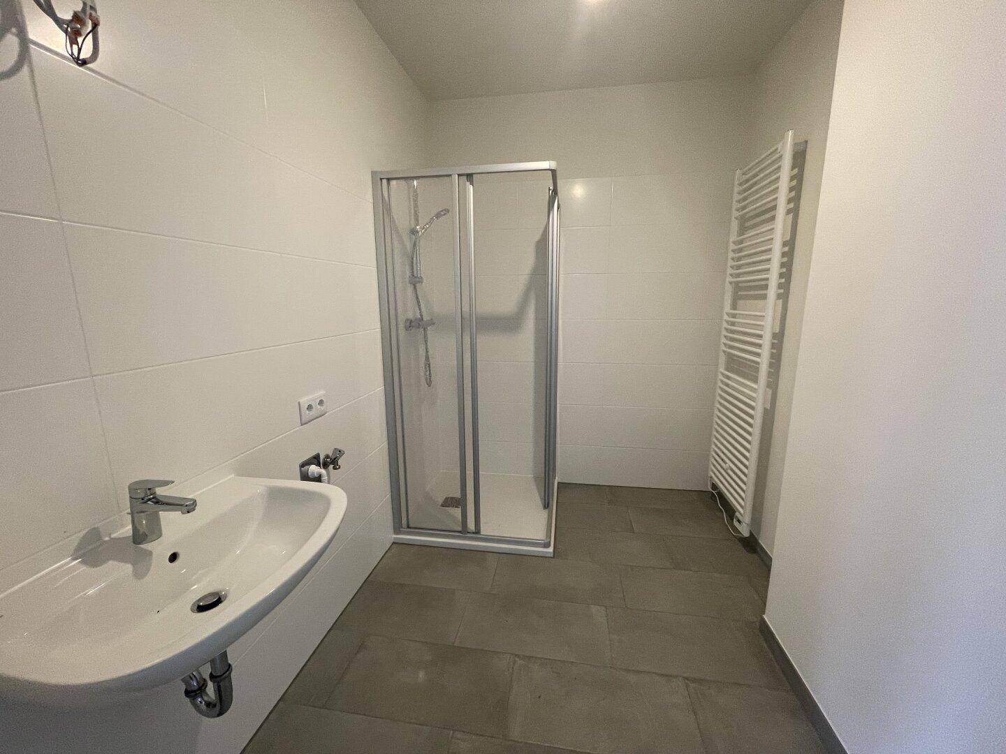 Modernes Badezimmer mit Duschkabine, Waschbecken und beheiztem Handtuchhalter.