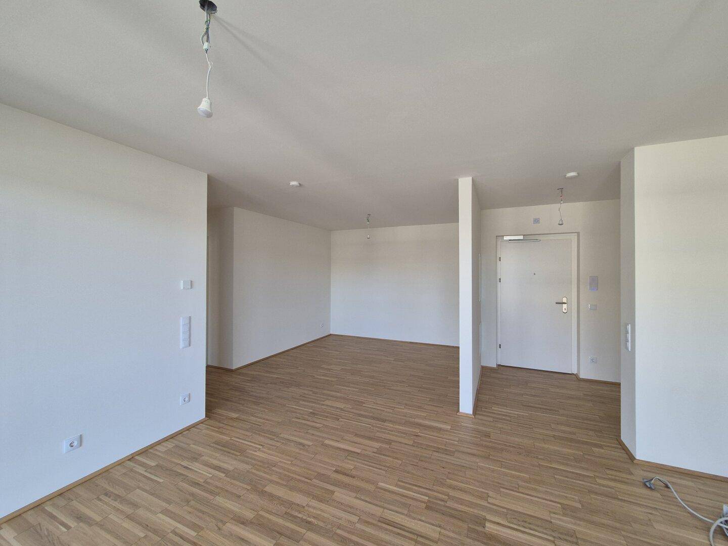 Leerer Wohnbereich mit Parkettboden und weißen Wänden, bereit für die individuelle Einrichtung.