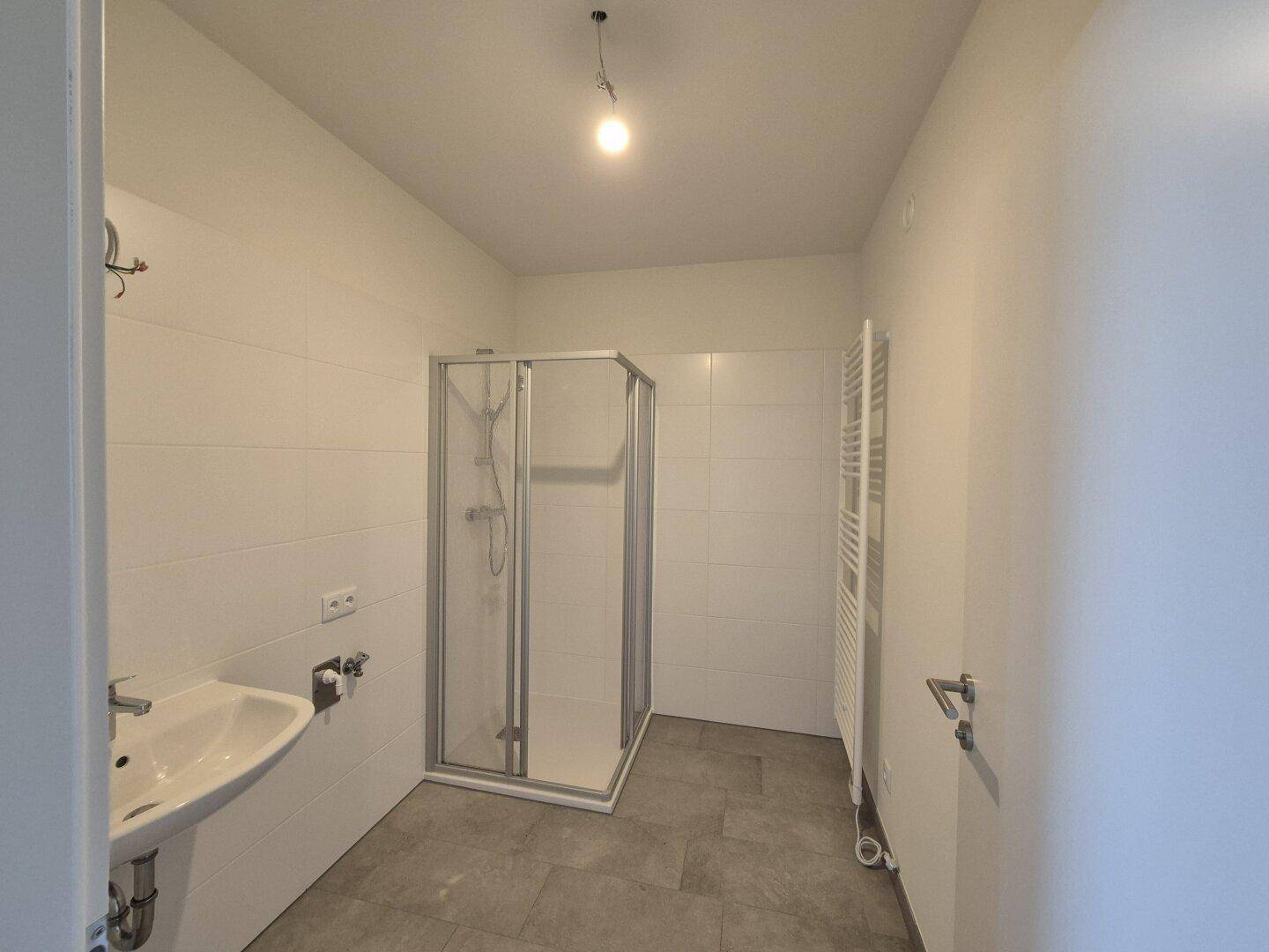 Helles Badezimmer mit Duschkabine, Waschbecken und beheiztem Handtuchhalter, modern gefliest.