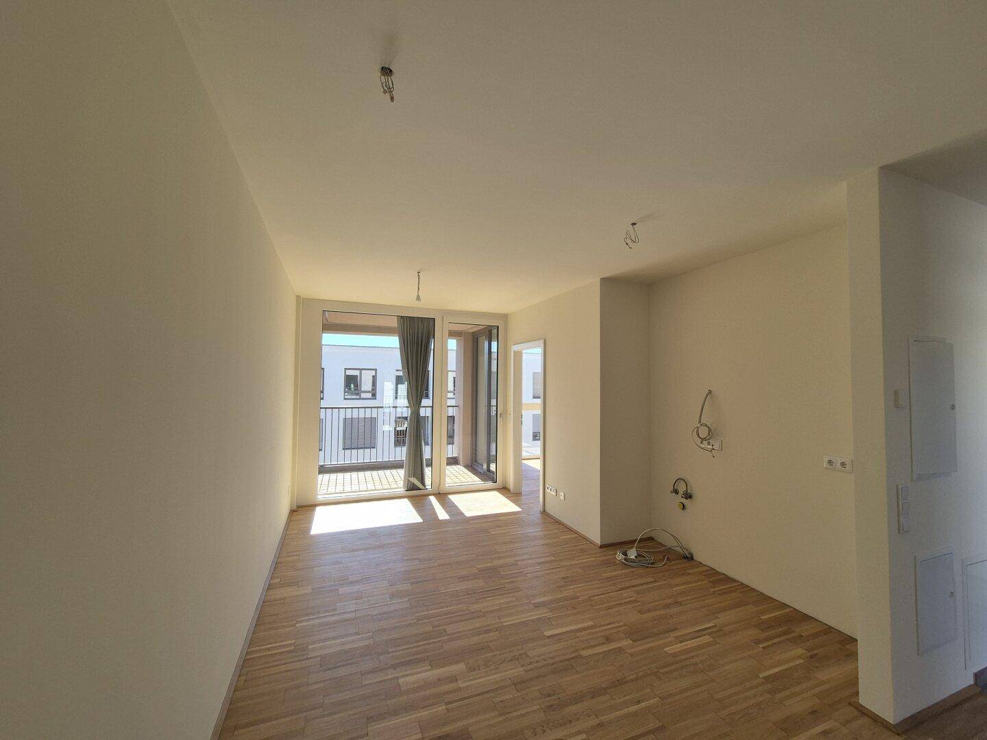 Lichtdurchflutetes Wohnzimmer mit Holzboden und Zugang zu einem Balkon, bereit zur Einrichtung.