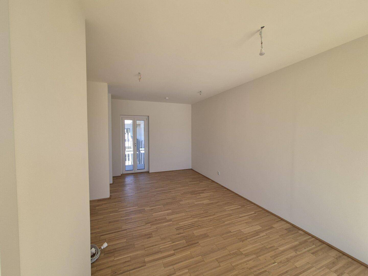 Geräumiges Wohnzimmer mit hellem Holzboden und viel Tageslicht, ideal für individuelle Gestaltung.