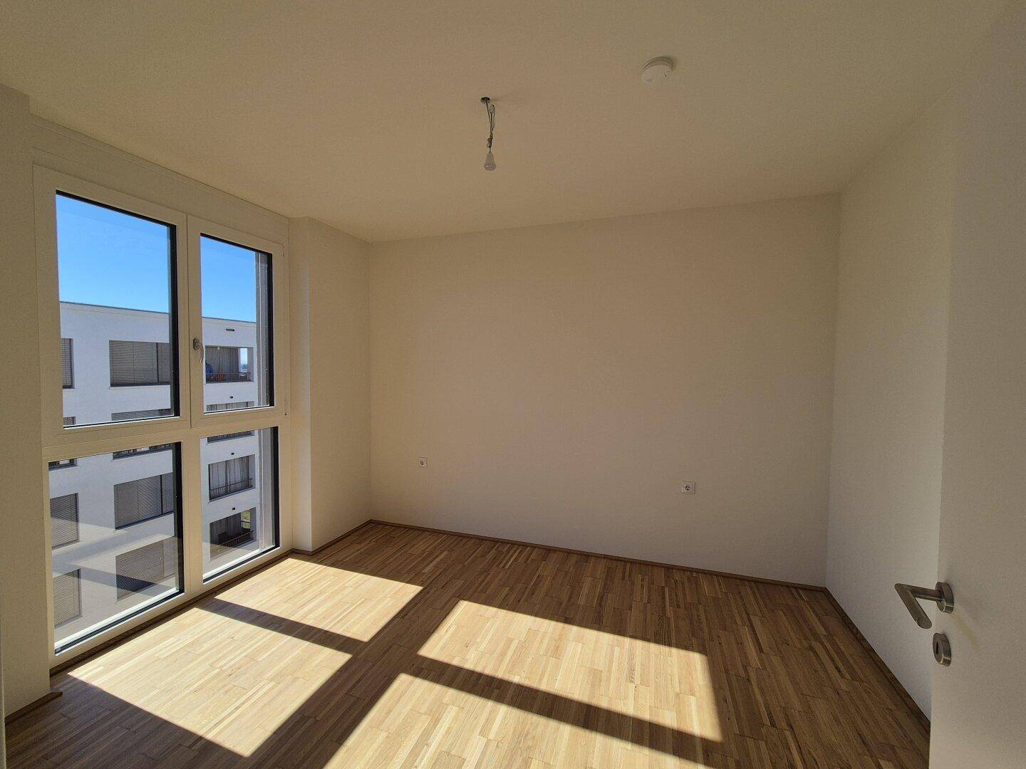 Helles Schlafzimmer mit Holzboden und großen Fenstern, die viel Tageslicht hereinlassen.
