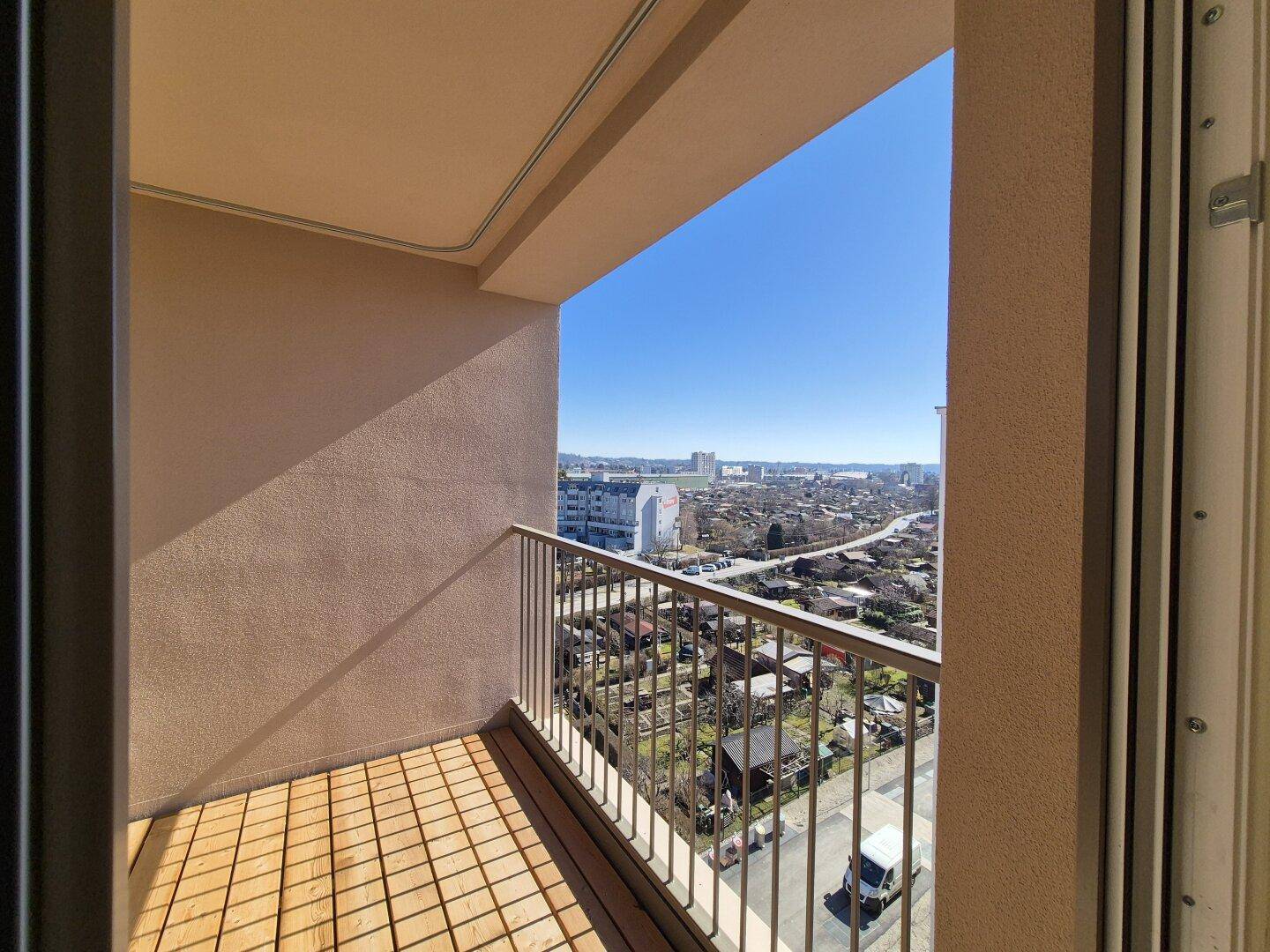 Geräumiger Balkon mit Holzboden und Panoramablick auf die Stadt und die grüne Umgebung.